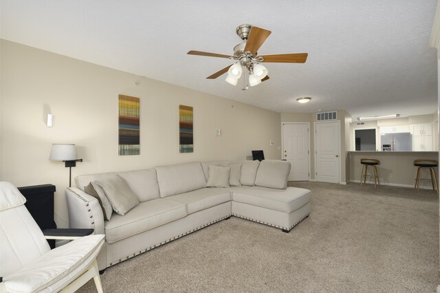 living room featuring a textured ceiling, light colored carpet, and ceiling fan