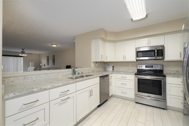 kitchen with sink, ceiling fan, white cabinetry, stainless steel appliances, and light stone counters