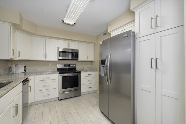 kitchen featuring white cabinetry, appliances with stainless steel finishes, light stone counters, and light hardwood / wood-style flooring