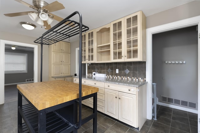 kitchen with cream cabinetry, dark tile patterned floors, light stone countertops, and backsplash