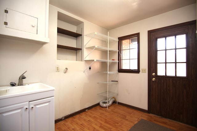 laundry area featuring cabinets, electric dryer hookup, sink, and light wood-type flooring