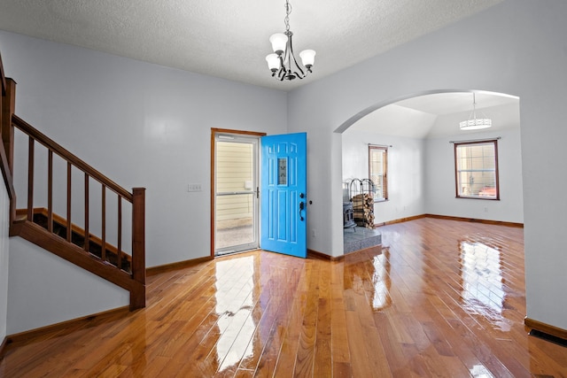 entrance foyer with vaulted ceiling, a textured ceiling, an inviting chandelier, and light hardwood / wood-style flooring