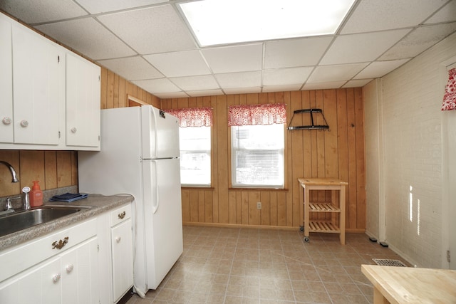 kitchen with sink, a paneled ceiling, white cabinets, and wood walls