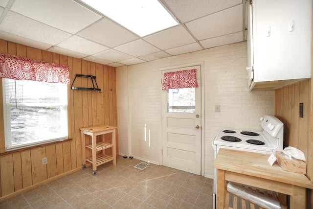 interior space with white electric stove, a drop ceiling, and wood walls