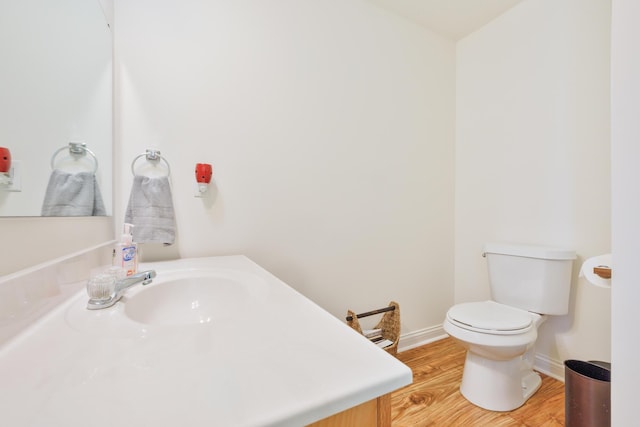 half bathroom with toilet, wood finished floors, baseboards, and a sink