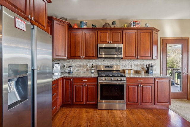 kitchen with appliances with stainless steel finishes, light wood-type flooring, light stone counters, and decorative backsplash