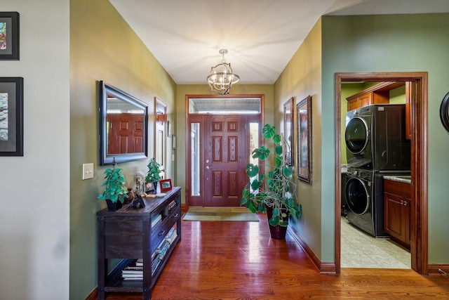 foyer entrance with stacked washer / dryer, light hardwood / wood-style floors, and a notable chandelier