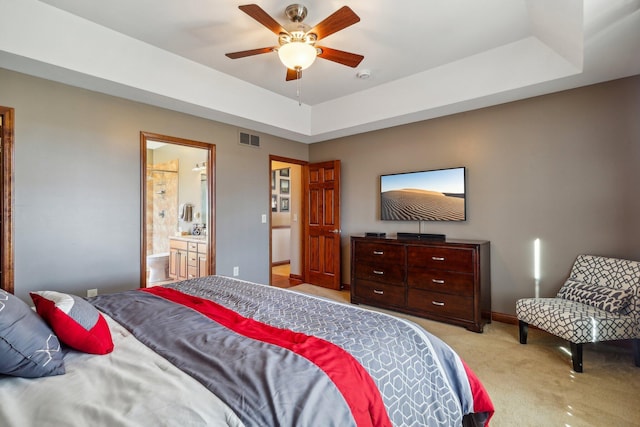 bedroom with ceiling fan, connected bathroom, a tray ceiling, and light carpet