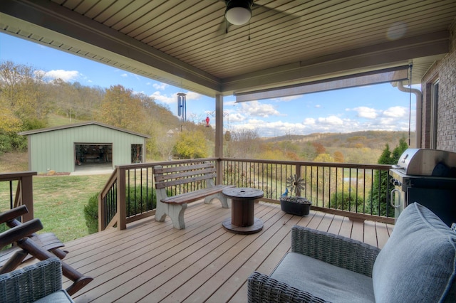 wooden terrace featuring area for grilling, an outdoor structure, and ceiling fan