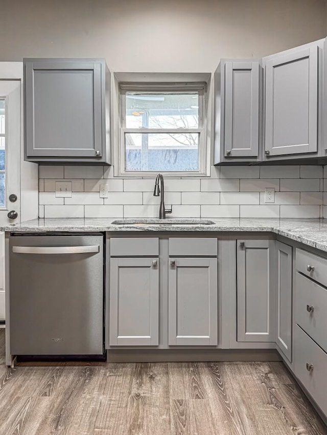 kitchen featuring stainless steel dishwasher, gray cabinets, sink, and light stone countertops