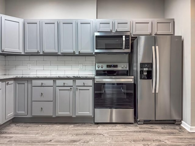 kitchen with stainless steel appliances, gray cabinets, light stone counters, and light hardwood / wood-style floors