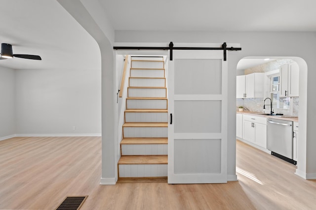 staircase featuring sink, wood-type flooring, a barn door, and ceiling fan