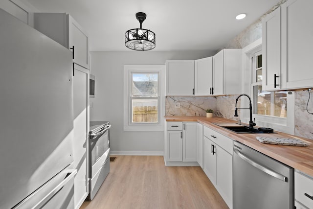 kitchen with sink, appliances with stainless steel finishes, white cabinetry, hanging light fixtures, and wood counters