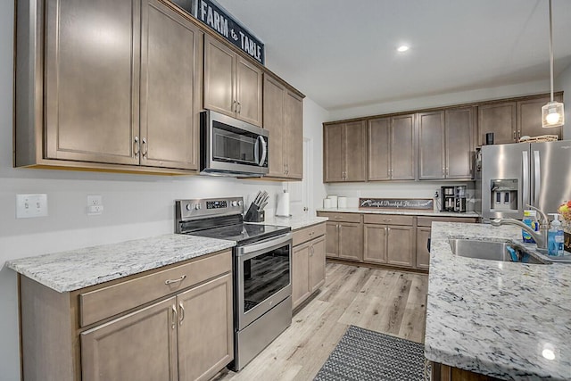 kitchen featuring decorative light fixtures, sink, stainless steel appliances, light stone countertops, and light wood-type flooring