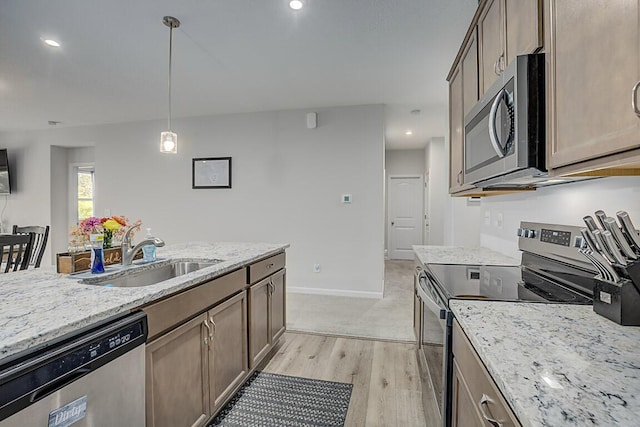 kitchen with sink, stainless steel appliances, light stone counters, decorative light fixtures, and light wood-type flooring