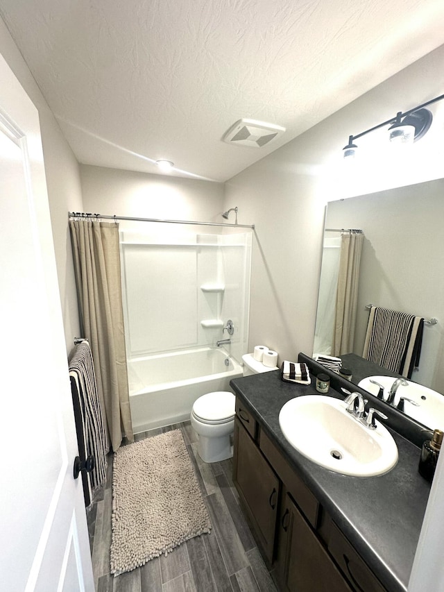 full bathroom featuring shower / tub combo with curtain, vanity, wood-type flooring, a textured ceiling, and toilet