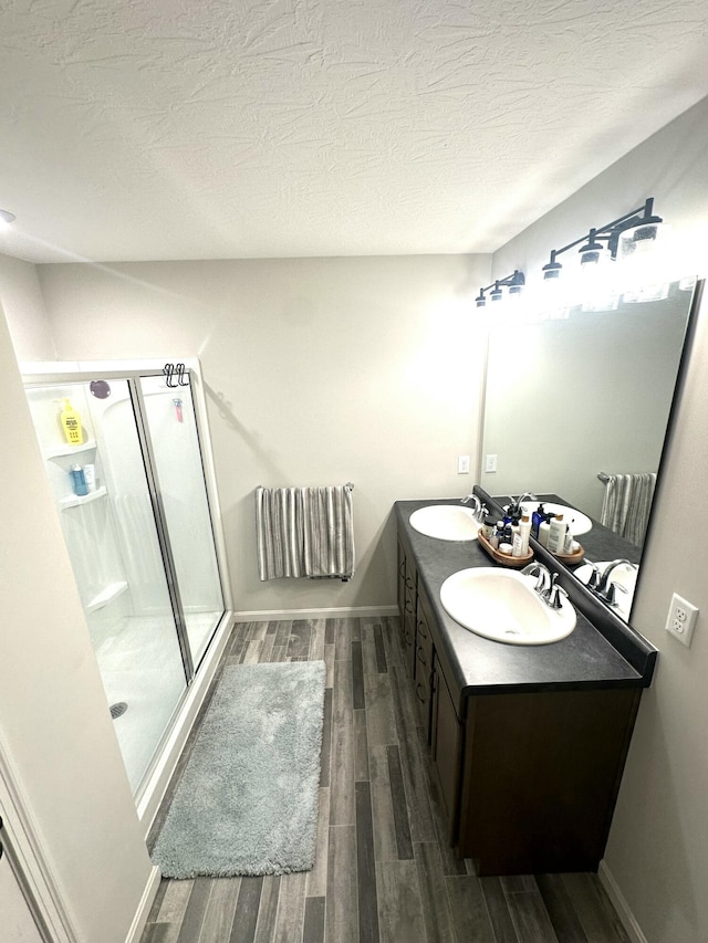 bathroom featuring wood-type flooring, a shower with door, vanity, and a textured ceiling