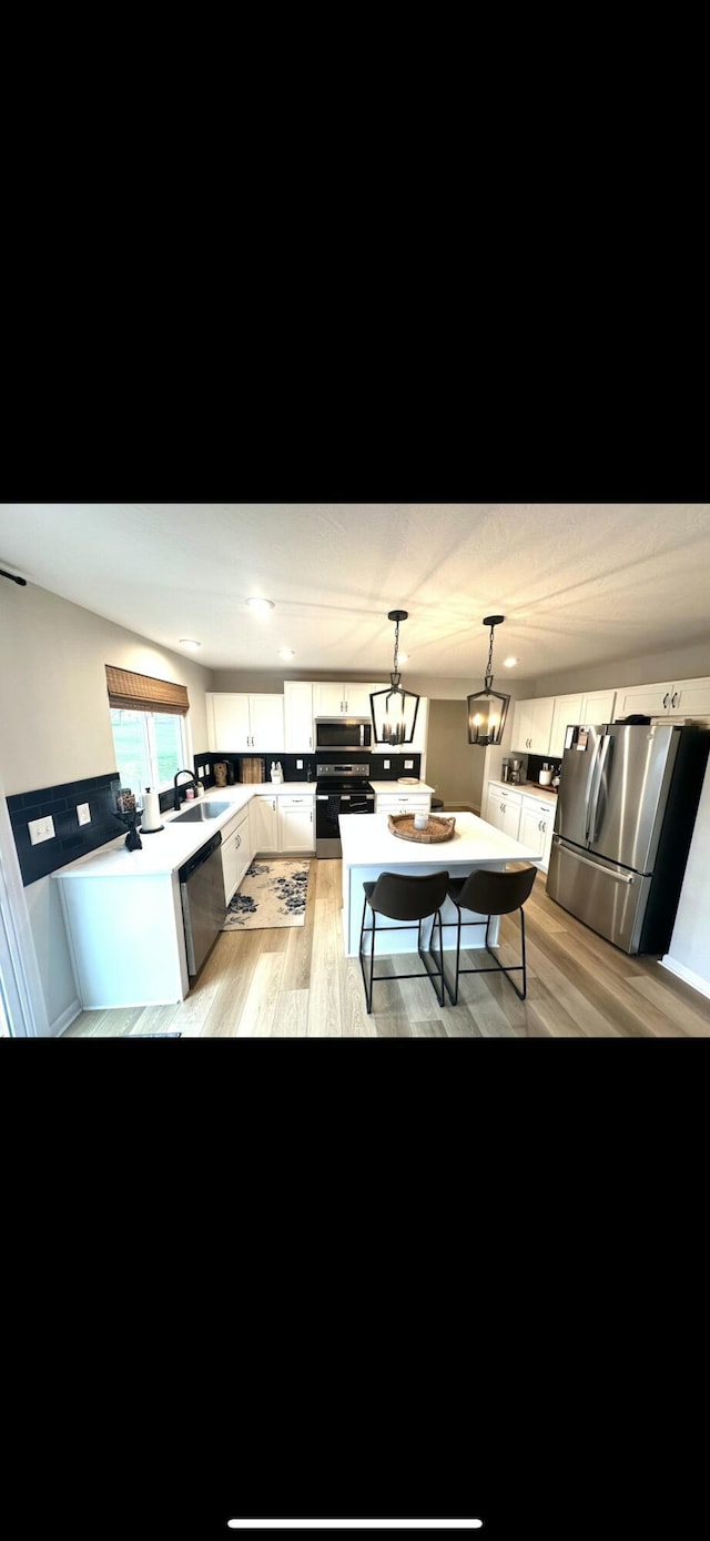 interior space featuring appliances with stainless steel finishes, pendant lighting, sink, white cabinets, and light hardwood / wood-style flooring