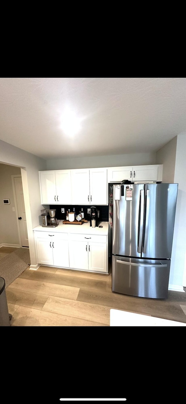 kitchen featuring stainless steel fridge, light hardwood / wood-style flooring, and white cabinets