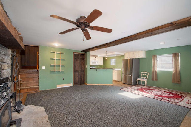 unfurnished living room with beamed ceiling, a stone fireplace, light carpet, and ceiling fan