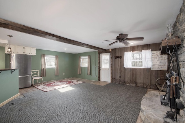 unfurnished living room featuring beamed ceiling, ceiling fan, and wooden walls