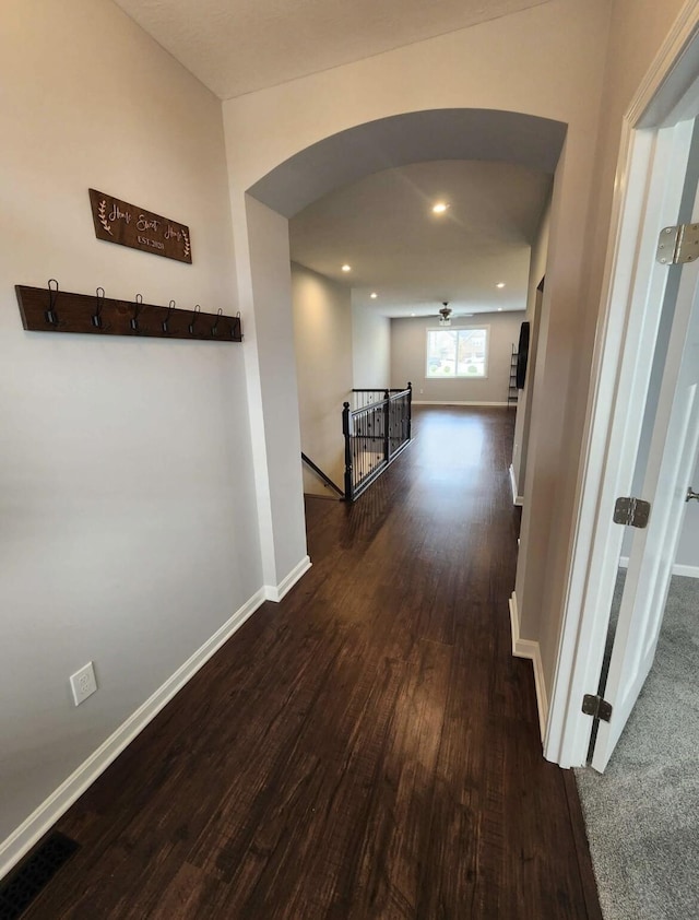 hallway with baseboards, recessed lighting, arched walkways, dark wood-type flooring, and an upstairs landing