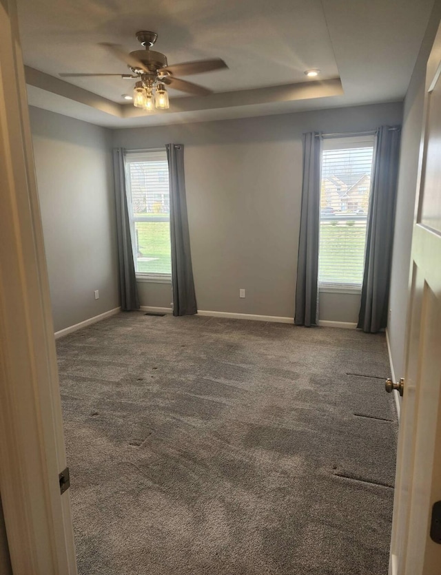 empty room with baseboards, a ceiling fan, a tray ceiling, and carpet floors