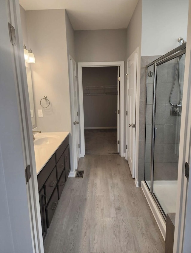 bathroom with a spacious closet, a shower stall, baseboards, wood finished floors, and vanity