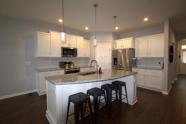 kitchen with a center island with sink, a sink, a kitchen breakfast bar, white cabinetry, and appliances with stainless steel finishes