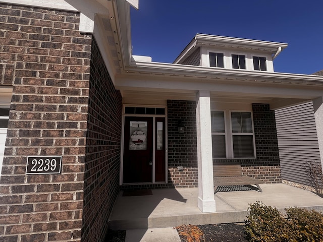 view of exterior entry featuring brick siding and covered porch