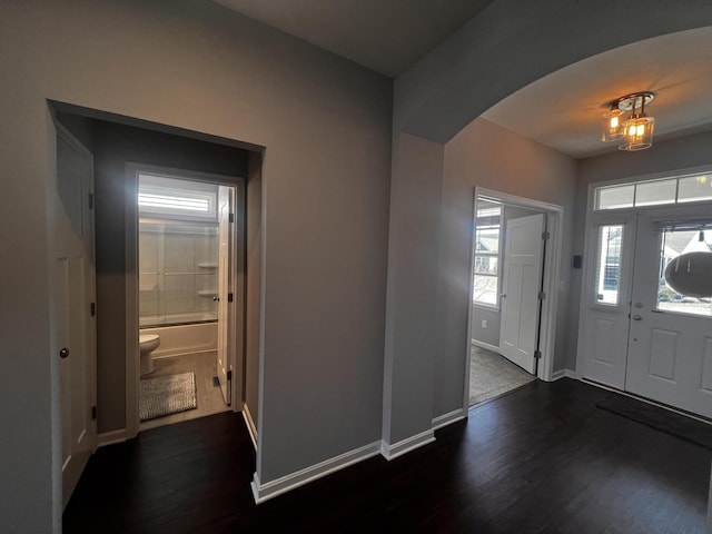 entrance foyer featuring baseboards, arched walkways, and dark wood-style flooring