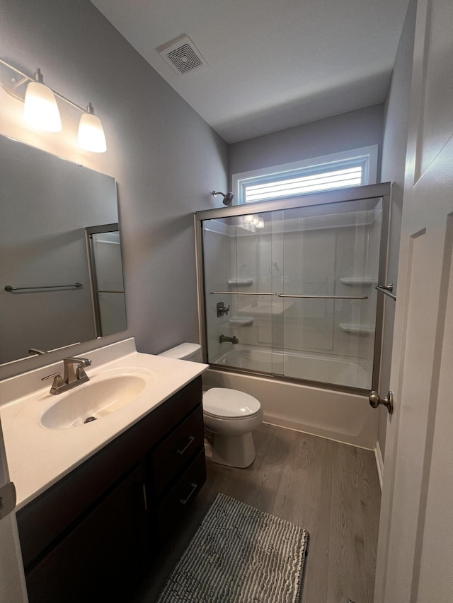 full bathroom with visible vents, toilet, wood finished floors, shower / bath combination with glass door, and vanity