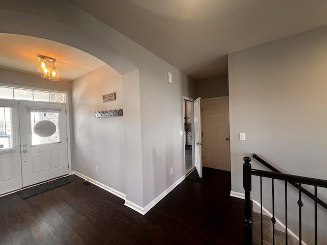 foyer entrance with baseboards, arched walkways, and wood finished floors