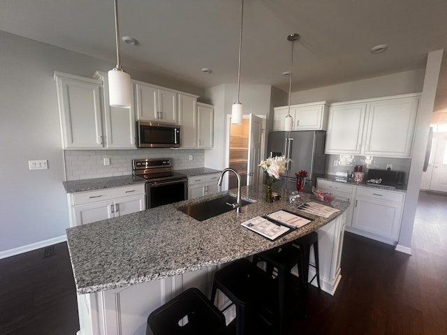 kitchen with a breakfast bar area, an island with sink, stainless steel appliances, white cabinetry, and a sink