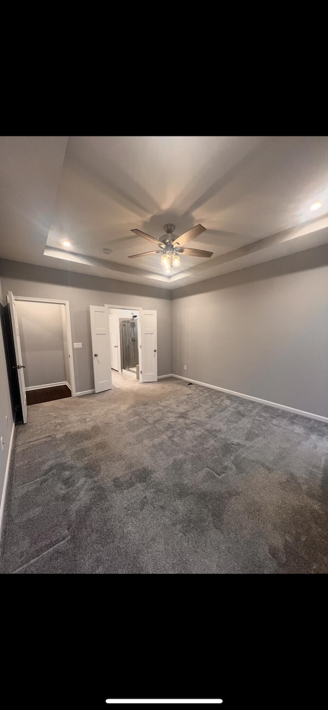 carpeted empty room with a tray ceiling, baseboards, and ceiling fan