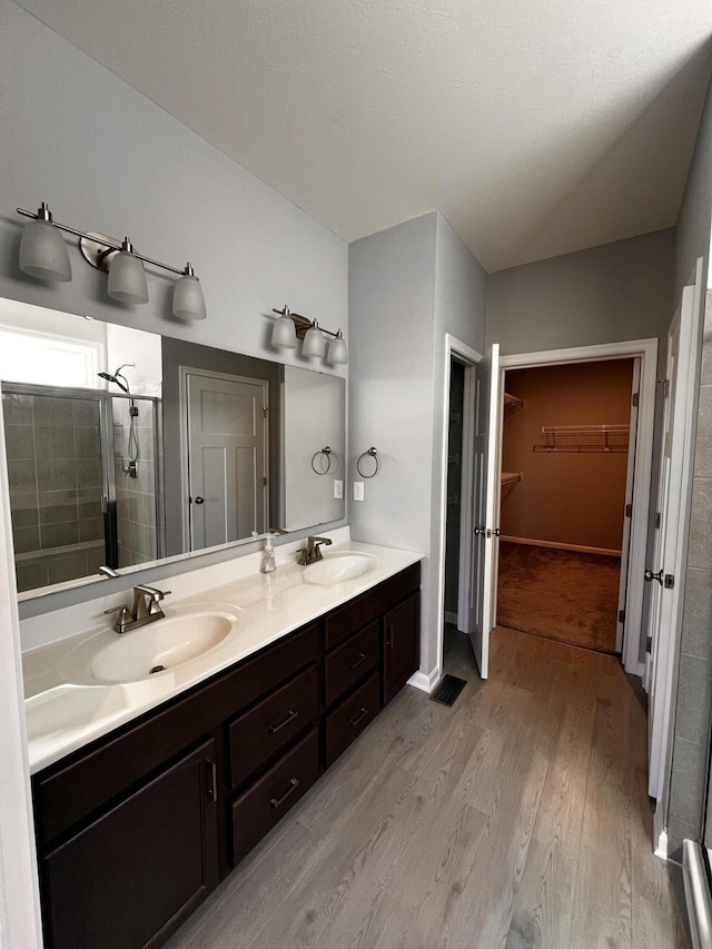 bathroom with a sink, wood finished floors, a stall shower, and double vanity