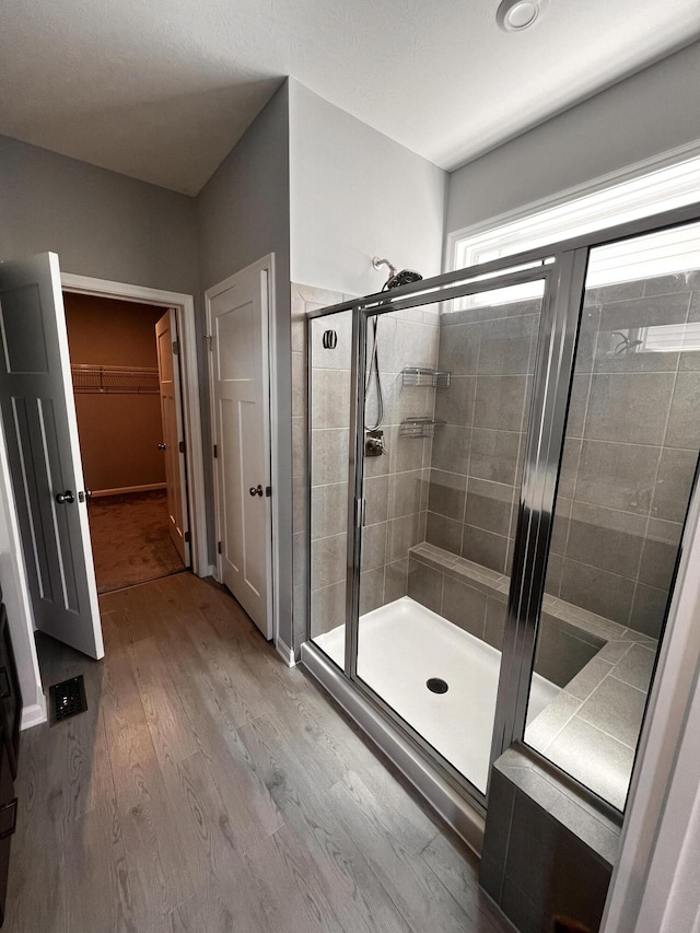 full bathroom featuring visible vents, a stall shower, a walk in closet, and wood finished floors