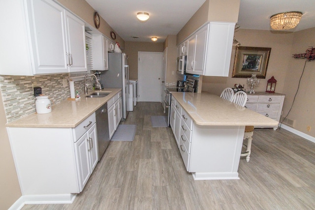 kitchen with sink, appliances with stainless steel finishes, white cabinetry, washing machine and dryer, and a kitchen bar