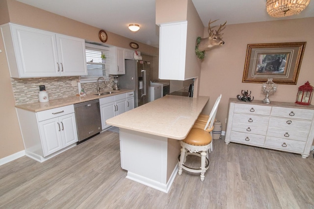 kitchen with sink, a breakfast bar area, appliances with stainless steel finishes, white cabinets, and light wood-type flooring