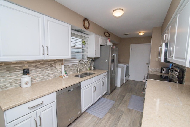 kitchen with stainless steel appliances, white cabinetry, separate washer and dryer, and sink