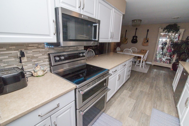 kitchen with stainless steel appliances, white cabinetry, backsplash, and light hardwood / wood-style flooring