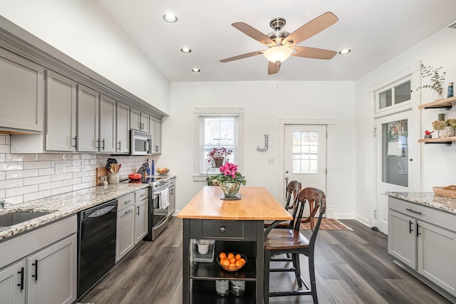 kitchen featuring dark wood-type flooring, tasteful backsplash, appliances with stainless steel finishes, gray cabinets, and light stone countertops