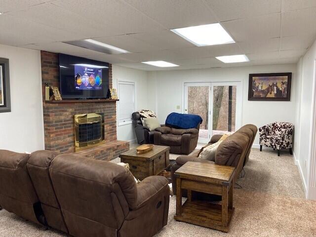 living room with light carpet, a fireplace, and a paneled ceiling