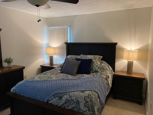 bedroom with ceiling fan, light colored carpet, and a textured ceiling