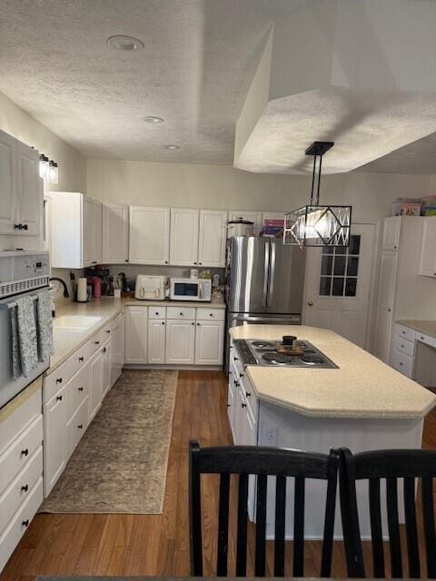 kitchen featuring pendant lighting, white cabinetry, stainless steel appliances, dark wood-type flooring, and a textured ceiling