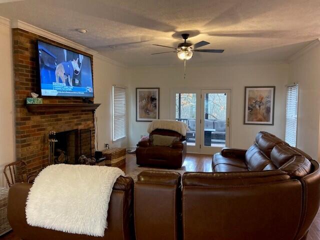 living room with hardwood / wood-style flooring, crown molding, a brick fireplace, and ceiling fan