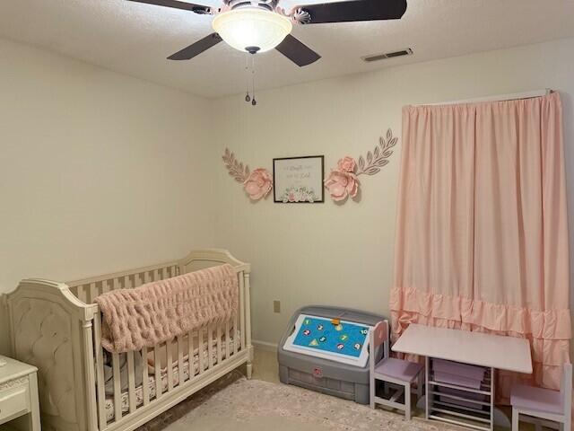 bedroom featuring a nursery area and ceiling fan