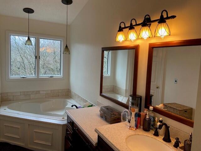 bathroom featuring vanity, a bath, and vaulted ceiling