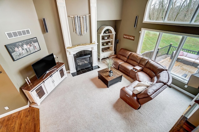 living room with a premium fireplace, carpet flooring, and a towering ceiling