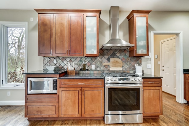 kitchen with decorative backsplash, light hardwood / wood-style flooring, stainless steel appliances, and wall chimney exhaust hood